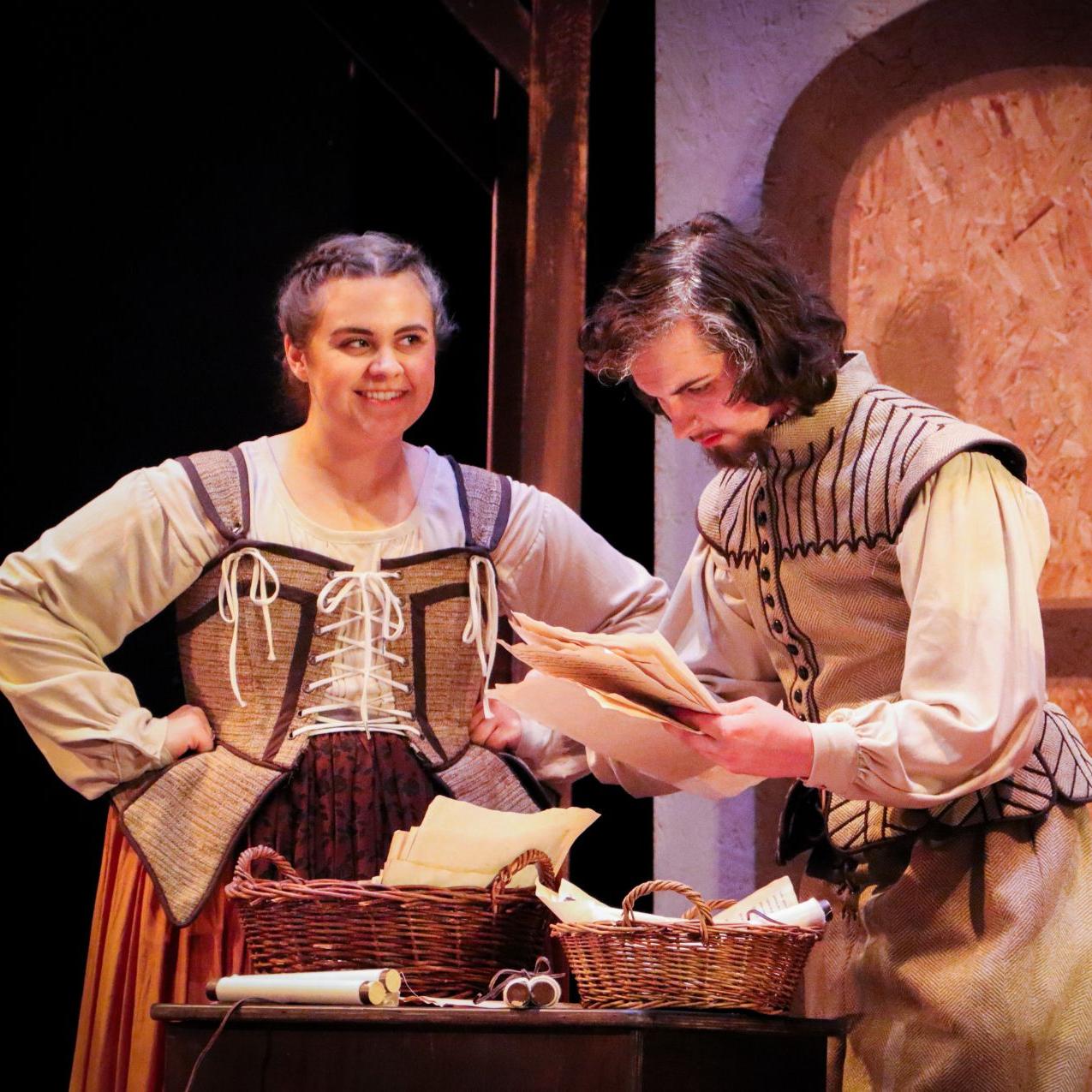 两个演员在舞台上表演《遗嘱之书》:一个年轻的男人和一个年轻的女人穿着伊丽莎白时代的衣服, 检查桌子上的一封信.