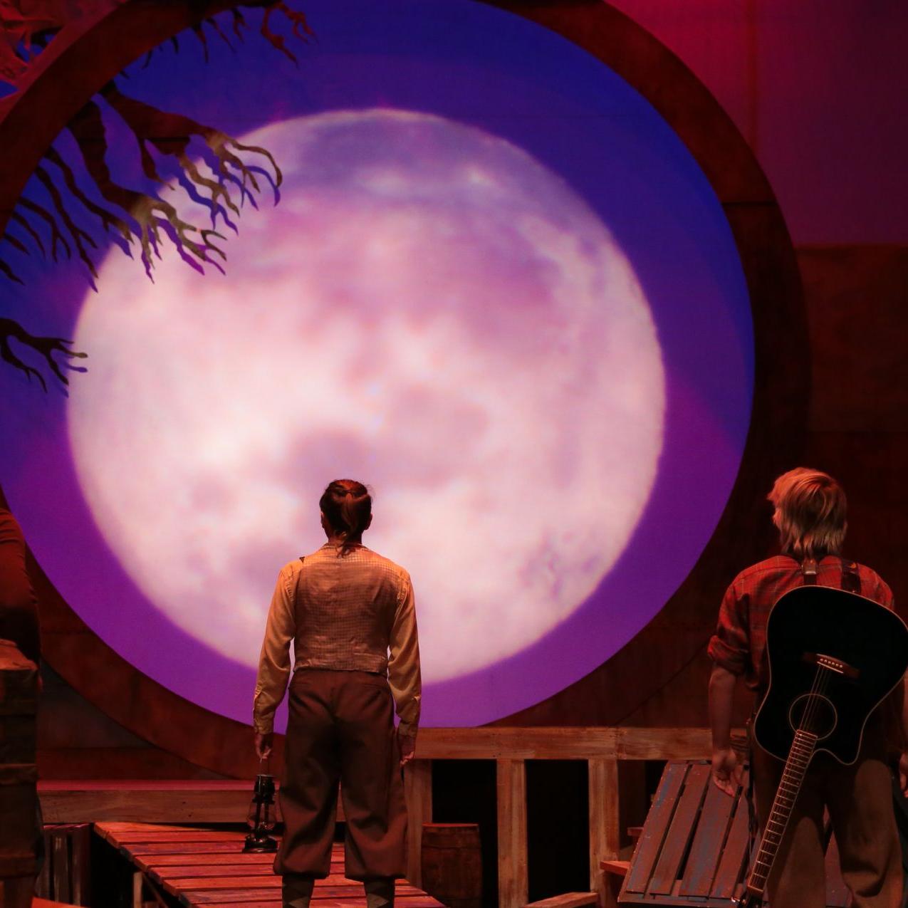 《爱德华·杜兰奇迹般的旅程》演出的舞台:背景被一个巨大的, 玫瑰色的月亮. 两个人面向月亮，朝月亮走去.