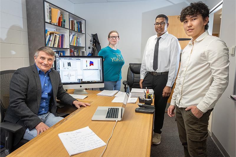 From left, Idaho State University students Bektur Akkabakov, Adil Ahmed, Isabella Dougherty, 和电子游戏平台教授Yury Gryazin在州立大学波卡特洛校区Gryazin的办公室里摆姿势拍照.