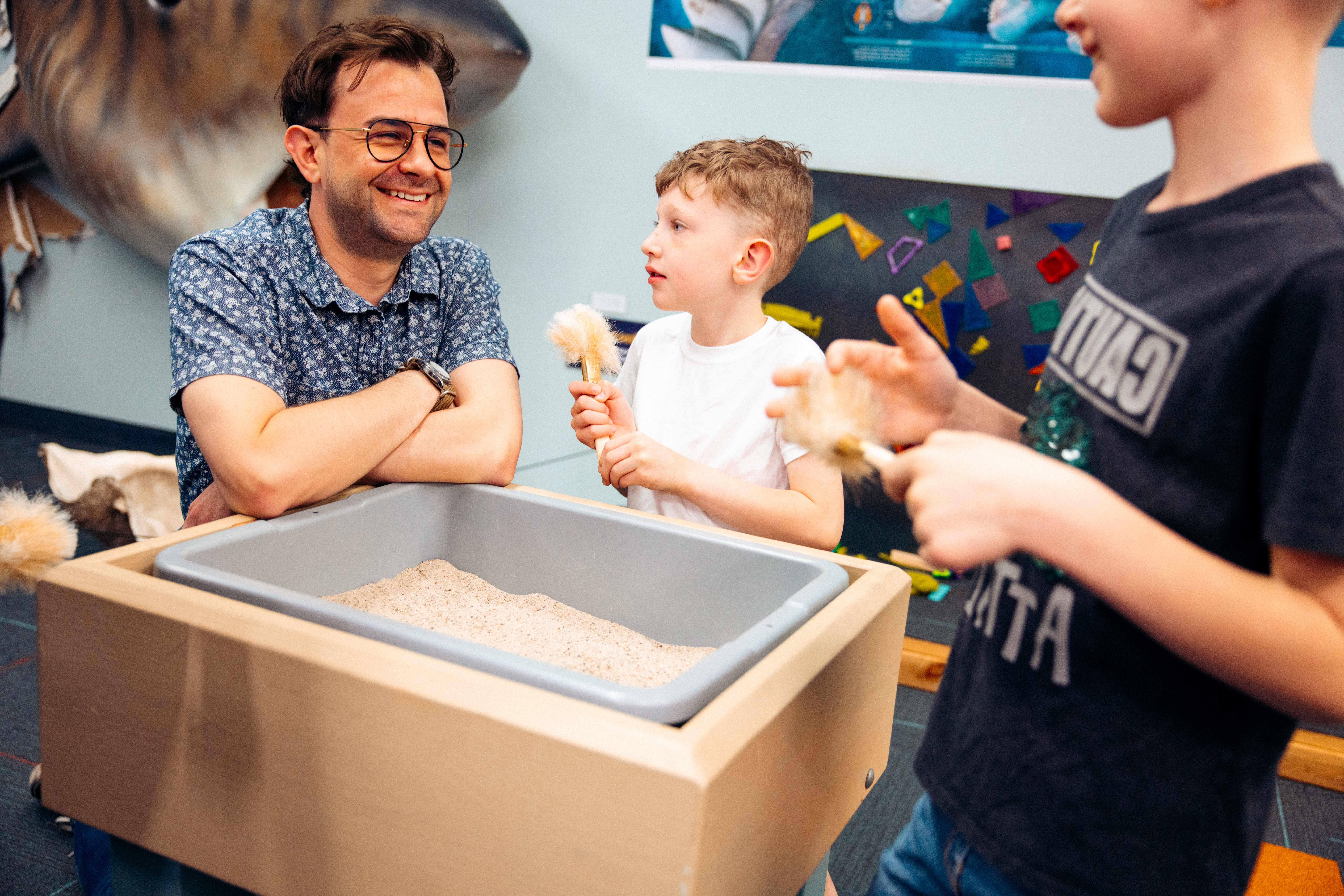 Father and two sons exploring a small fossil excavation box